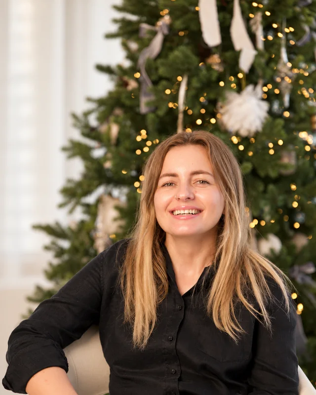 Melozina smiling in a black shirt, sitting in front of a lit Christmas tree