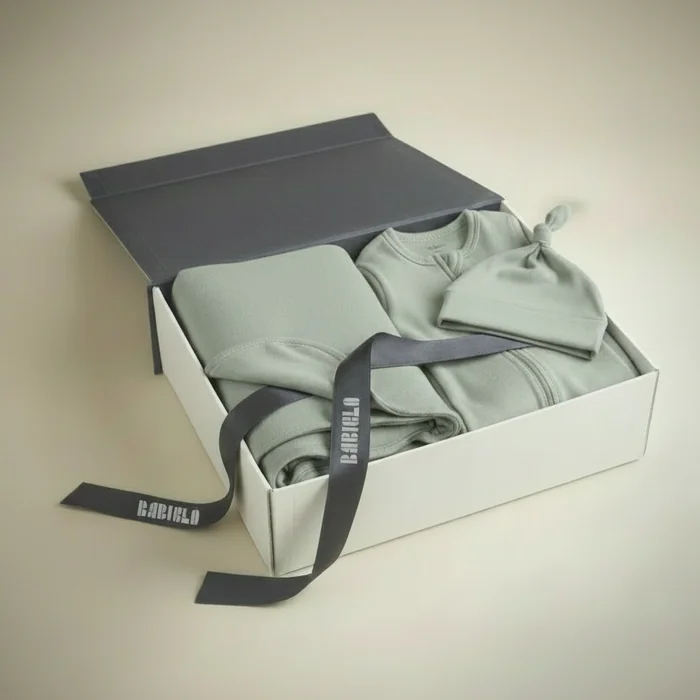 An open gift box of sage green baby clothes and a knotted hat, tied with a ribbon