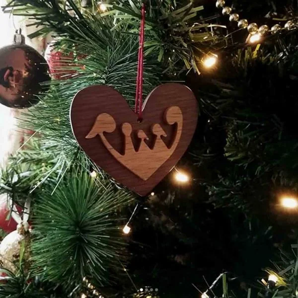 A wooden heart ornament with a cut-out family of three, hanging on a lit Christmas tree