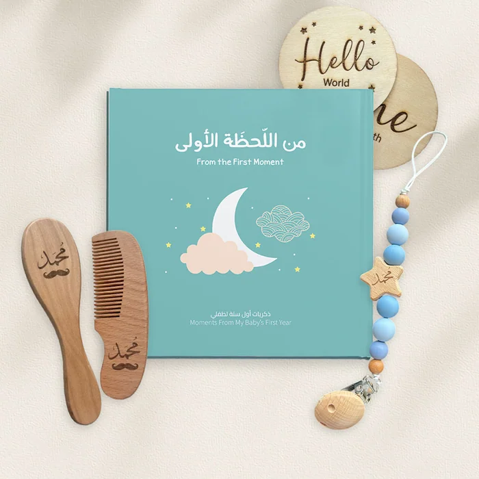 A baby keepsake set: an Arabic first-moments book, a name-engraved wooden brush and comb, and a dummy clip