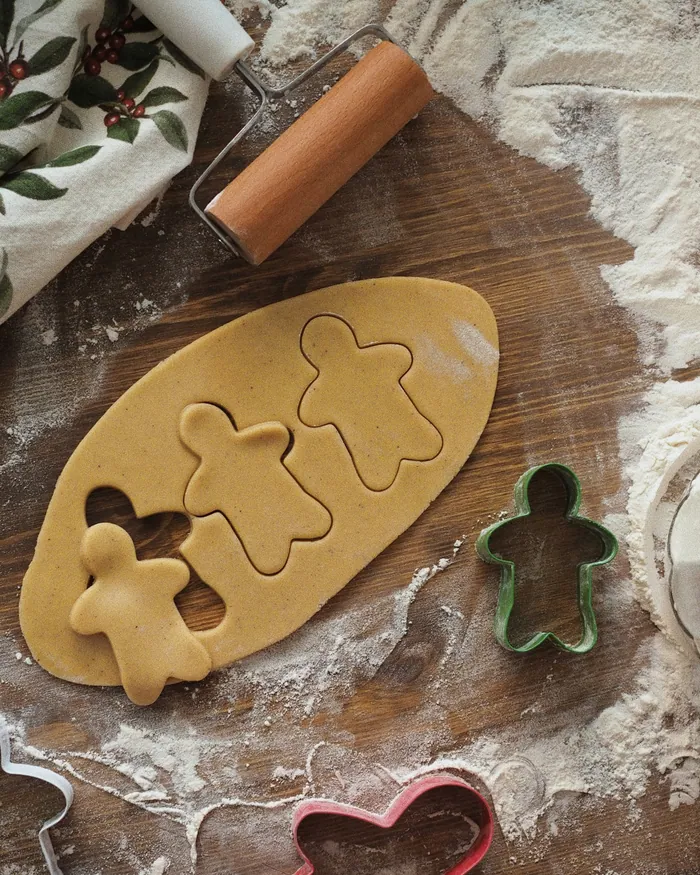 Gingerbread dough rolled out on a floured board with gingerbread-man cutters and a rolling pin