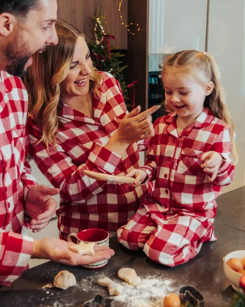 A mother and daughter in red gingham pyjamas laughing over the baking counter, flour everywhere