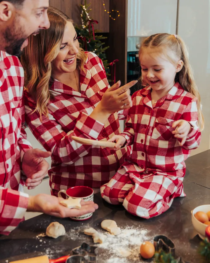 A mother and daughter in red gingham pyjamas laughing over the baking counter, flour everywhere