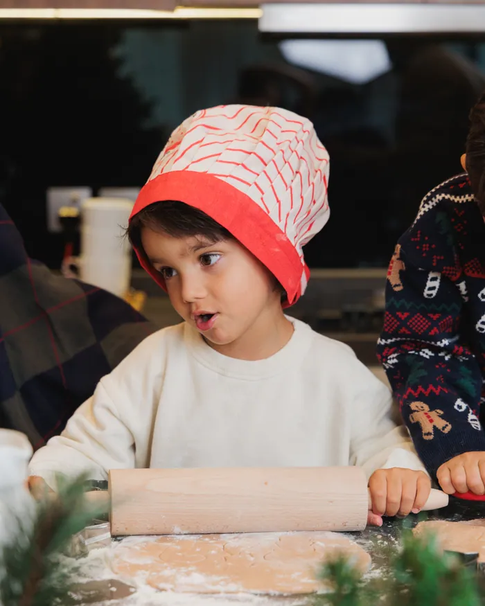 A boy in a red knitted hat with a rolling pin, flour everywhere