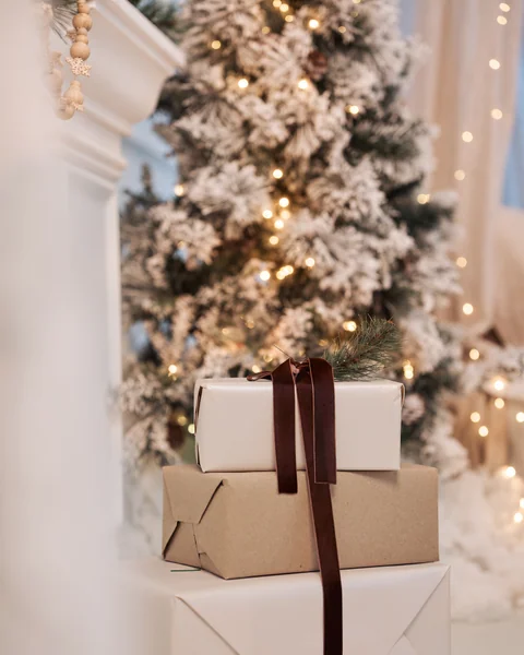 Presents tied with brown velvet ribbon stacked in front of a frosted tree and a white fireplace
