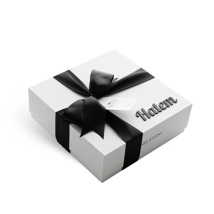 A white gift box tied with a black satin bow, the name Hatem raised in 3D letters on the lid