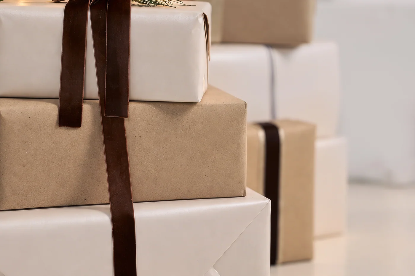 A stack of presents wrapped in white and brown paper and tied with dark brown velvet ribbon