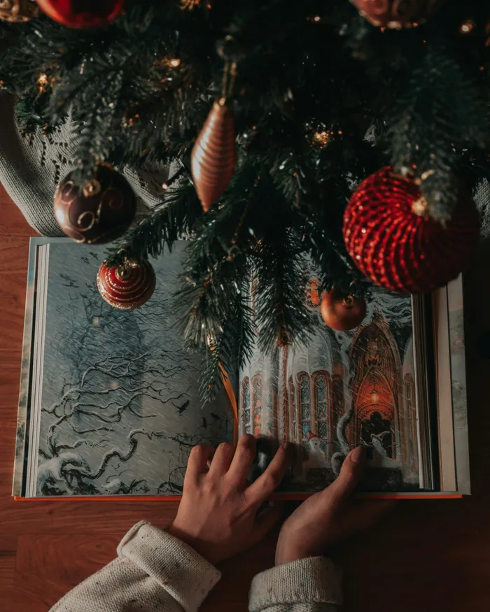 Hands turning the pages of an illustrated book beneath the branches of a Christmas tree