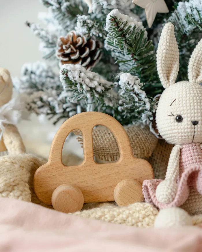 A wooden toy car beside a small crocheted bunny under a frosted Christmas tree