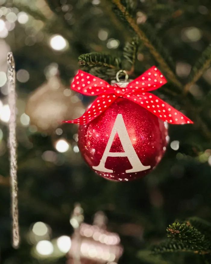 A red bauble with a white initial A tied with a red ribbon, hanging on a Christmas tree