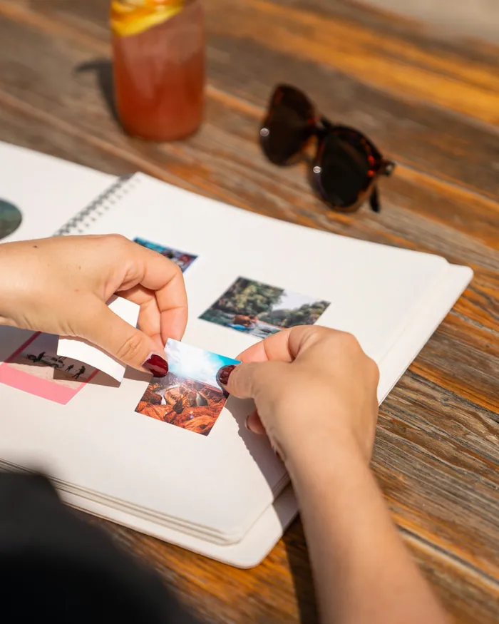 Hands pressing printed photographs into a white photo album on a wooden table