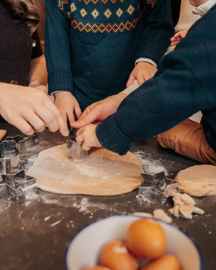 Small hands pressing a cutter into rolled-out dough on a dark counter, a bowl of eggs beside them