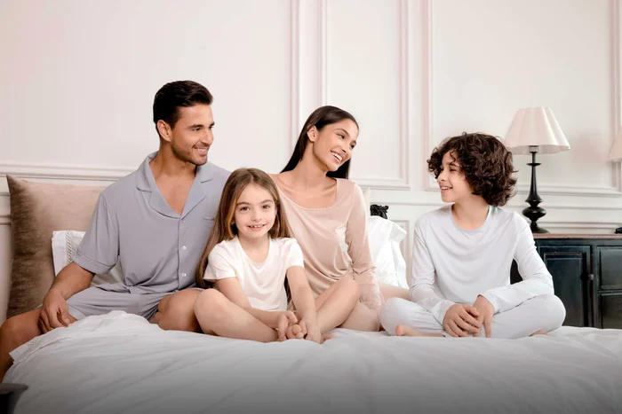 A father, mother and two children in soft loungewear sitting together on a white bed