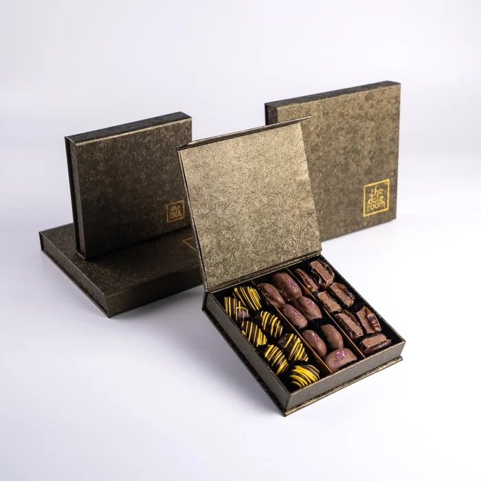 An open dark green Al Yered box of chocolate-dipped dates, two closed boxes behind it