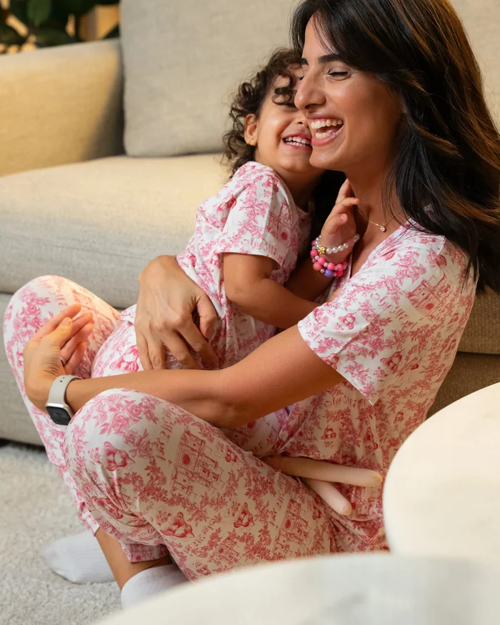 A mother and daughter laughing on the floor in matching pink floral pyjamas