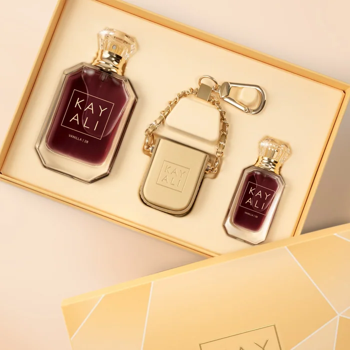 A Kayali gift set in an open gold box: two deep red perfume bottles and a gold bag charm