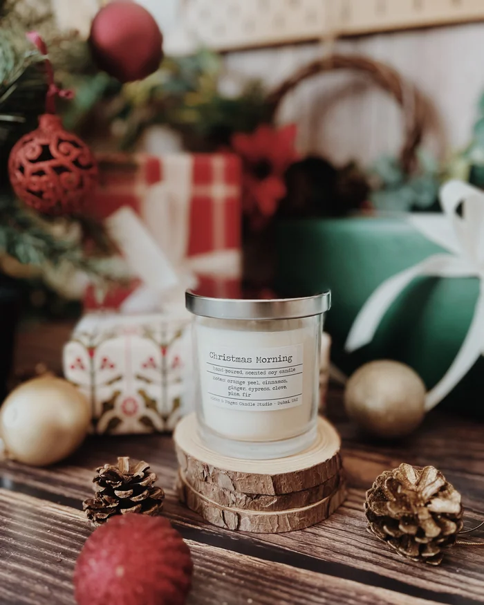 A candle in a glass jar on a wooden slice among baubles, pine cones and wrapped presents