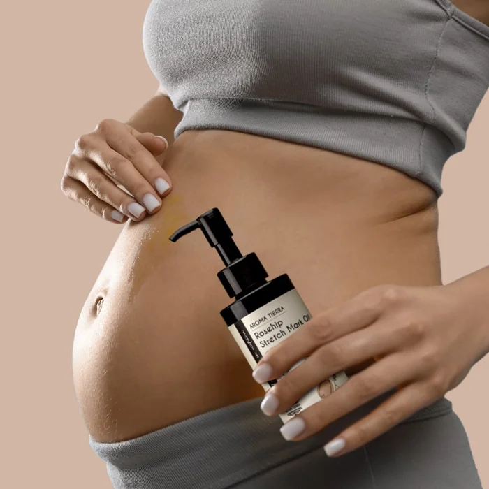 A pregnant woman holding a black pump bottle of Aroma Tierra rosehip oil against her bump