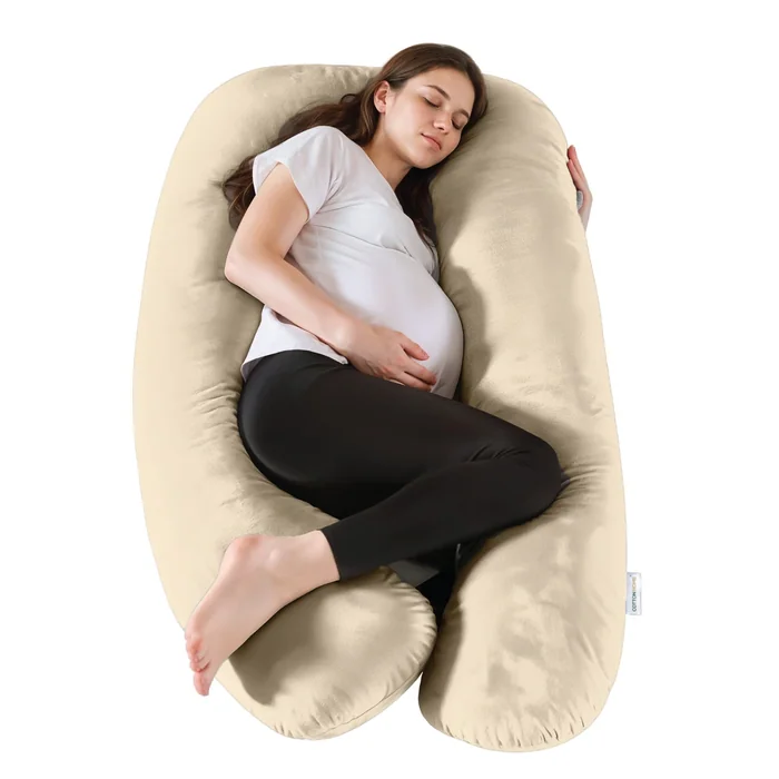 A pregnant woman asleep on her side, wrapped around a large cream U-shaped pillow