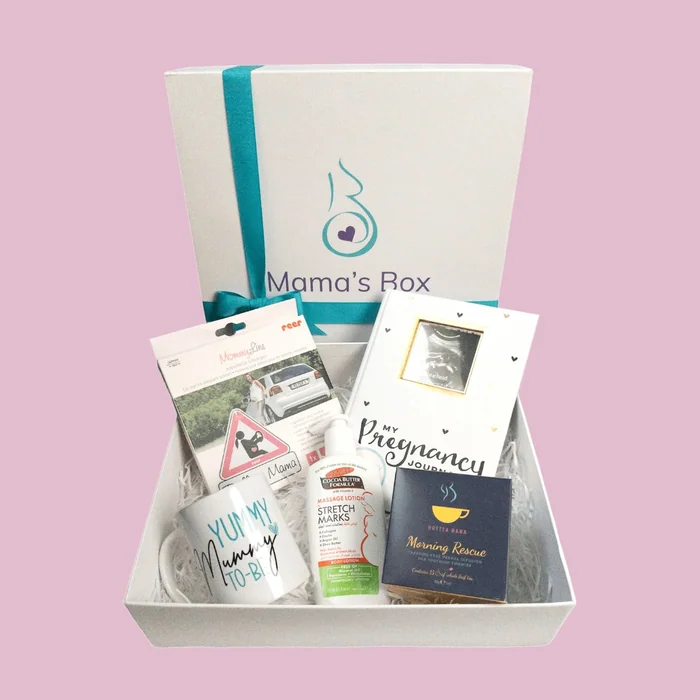 An open white Mama's Box with a pregnancy journal, a Yummy Mummy-to-be mug, a lotion, tea and a car sign