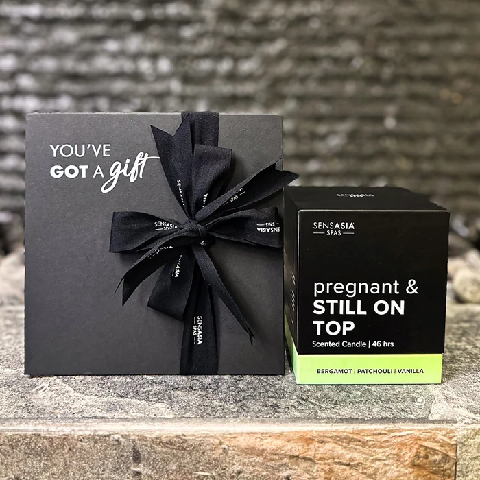 A black gift box tied with a black ribbon beside a boxed candle labelled Pregnant and Still On Top