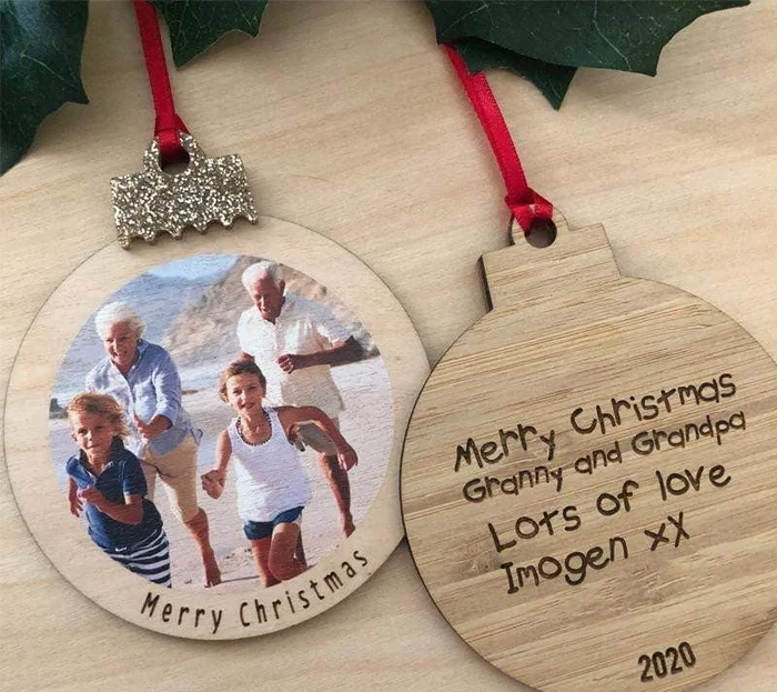 Two wooden baubles on red ribbons, one with a family photo and Merry Christmas, the other engraved with a message to grandparents