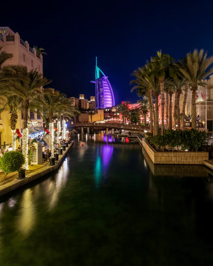 The canals of Madinat Jumeirah lit up at night, the Burj Al Arab glowing behind the palms