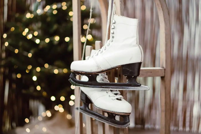 A pair of white ice skates hanging by their laces in front of Christmas lights