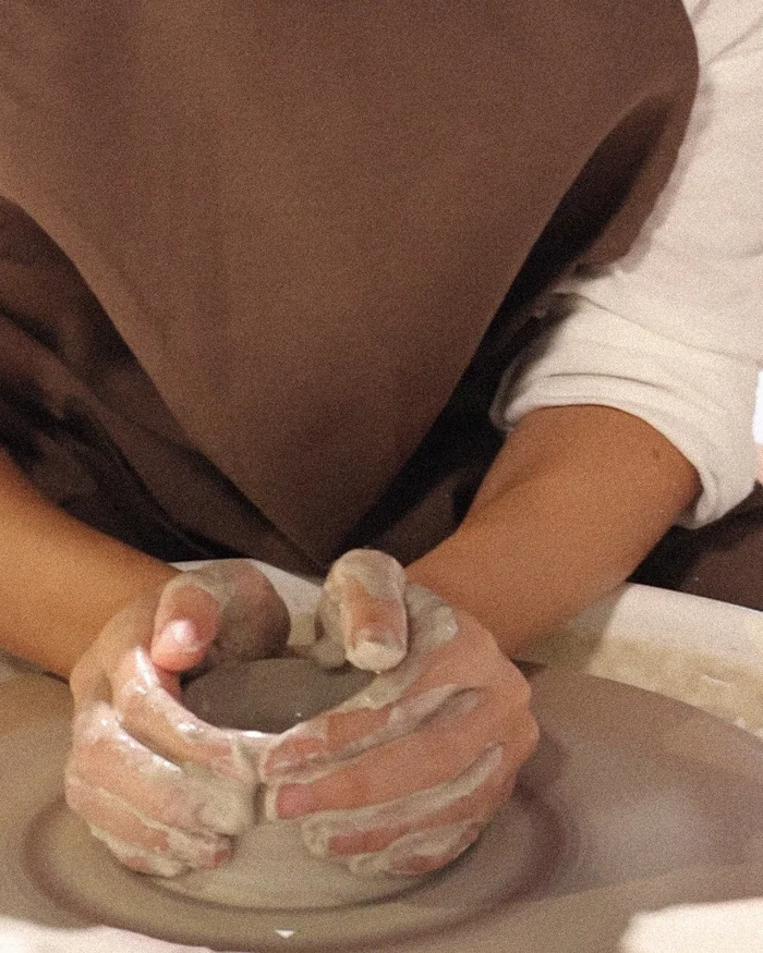Clay-covered hands shaping a pot on a potter's wheel