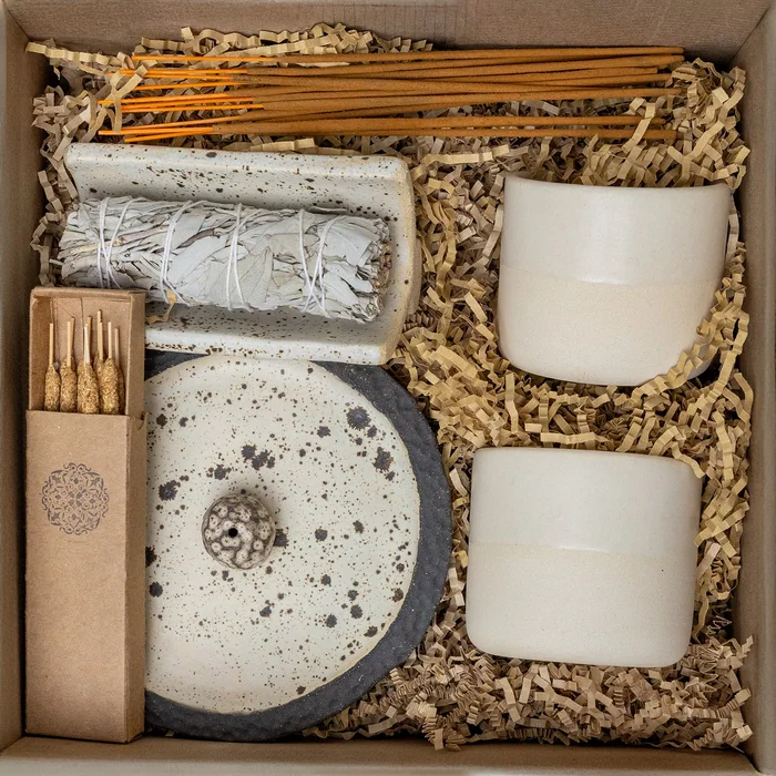 A gift box of ceramic cups, an incense holder, incense sticks and matches nestled in paper shred