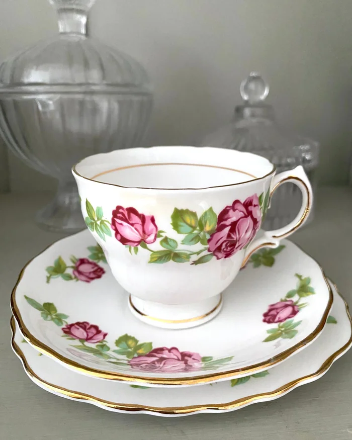 A vintage bone china teacup, saucer and plate painted with pink roses and finished with gold rims