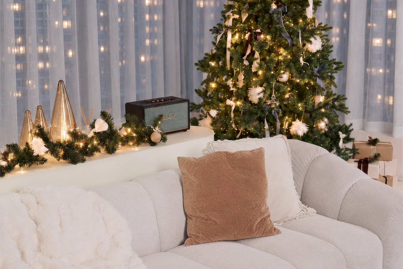 A cream sofa with a velvet cushion and a knitted throw beside a decorated Christmas tree and wrapped gifts