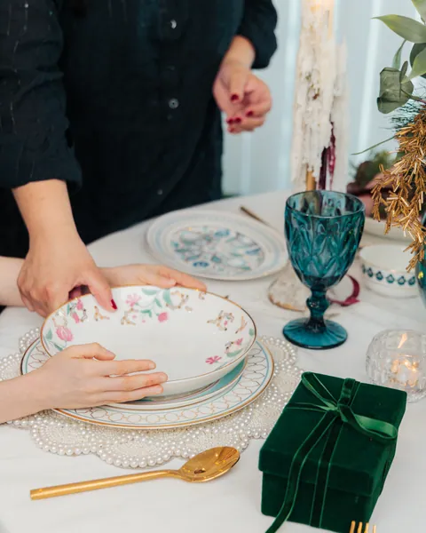 An adult and a child setting a floral bowl on a Christmas table beside a green velvet gift box