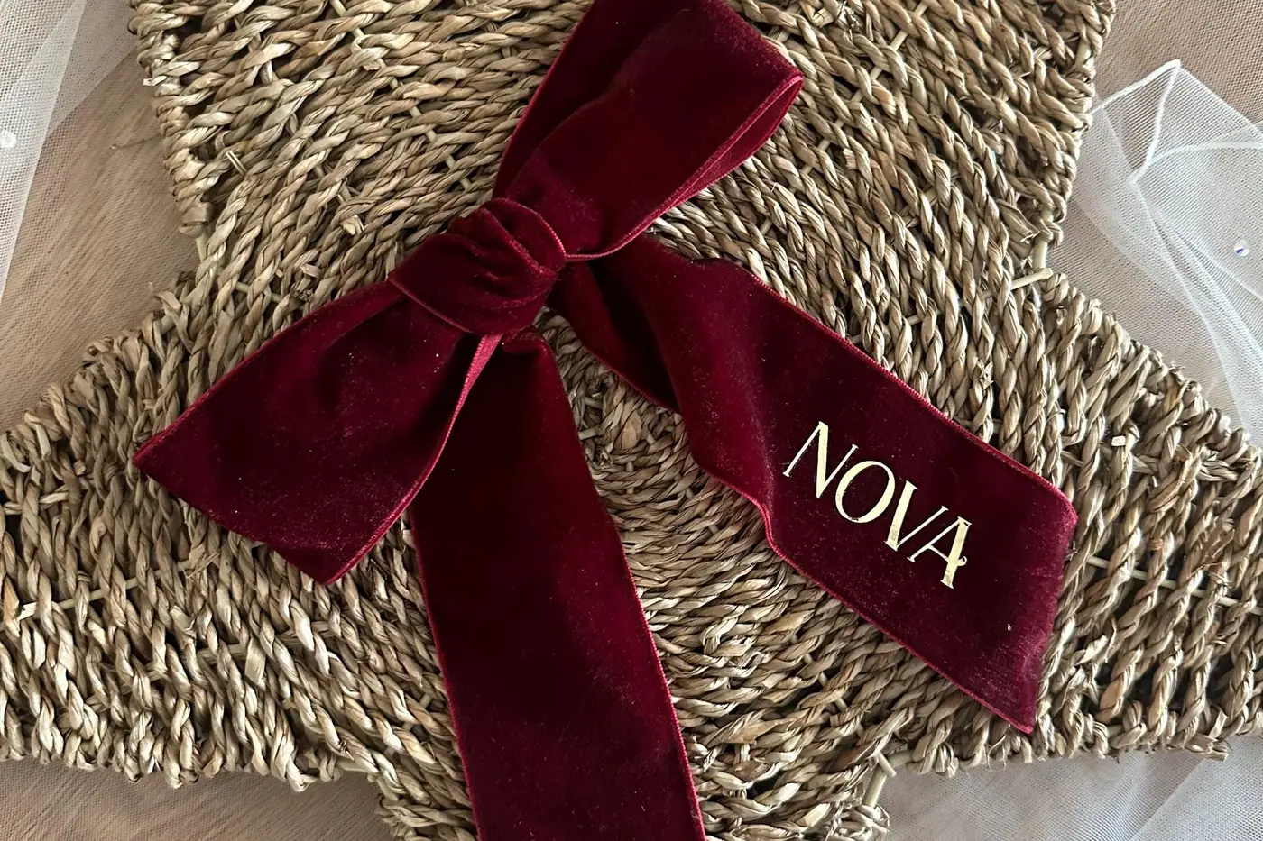 A woven star ornament tied with a burgundy velvet bow embroidered with the name Nova