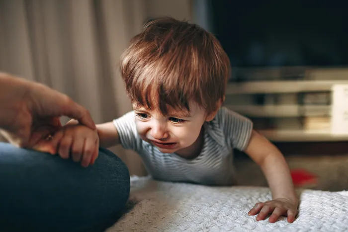 A toddler in a striped T-shirt crying on the floor, one hand pressed to the carpet