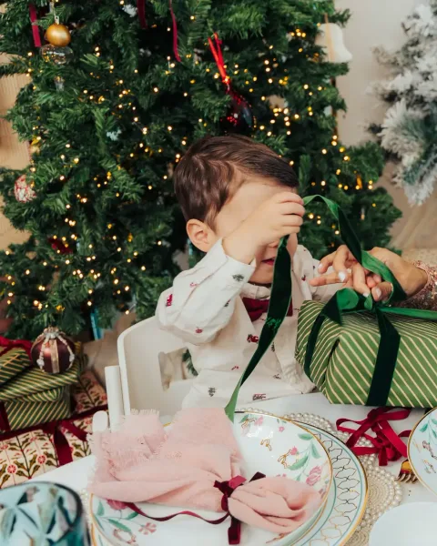 A mother and her young son unwrapping a green striped present at a laid Christmas table