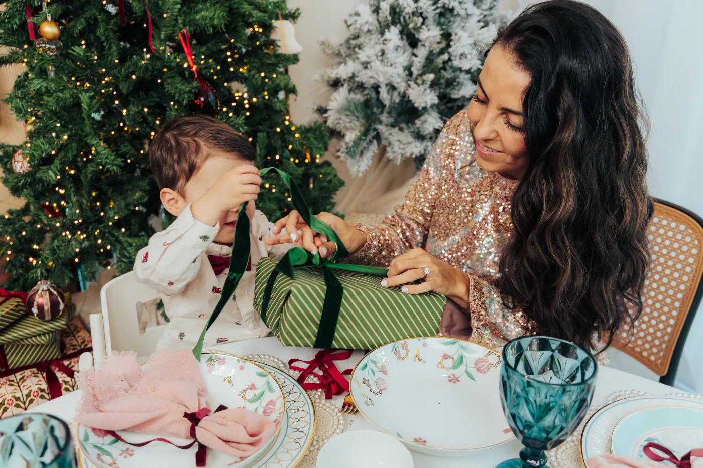 A mother and her young son unwrapping a green striped present at a laid Christmas table