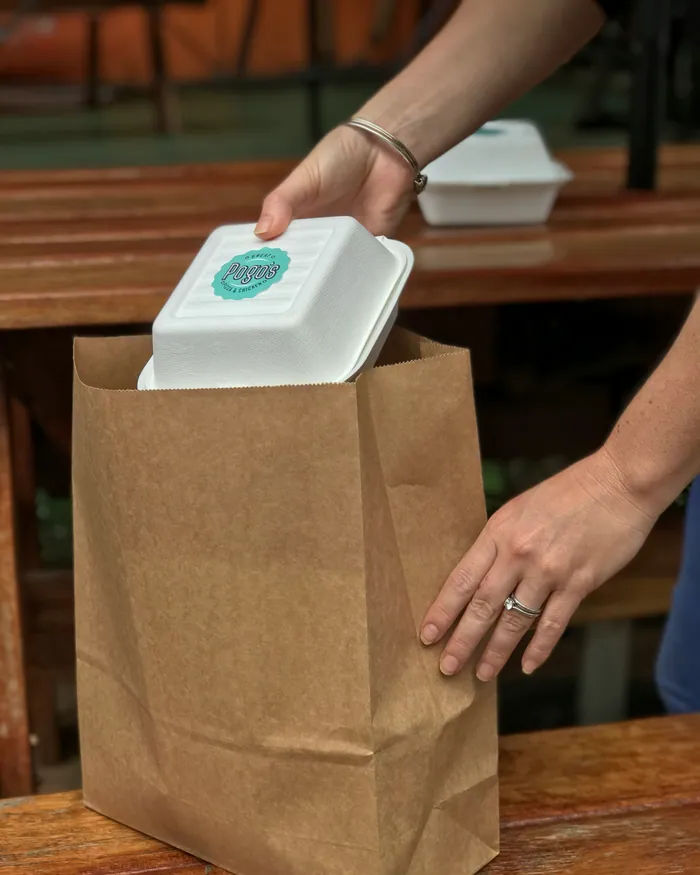 Hands lifting a takeaway container into a brown paper bag at a counter