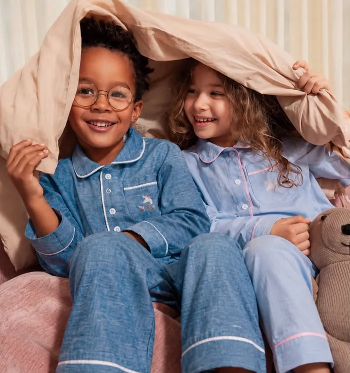 A boy and a girl in matching blue pyjamas sitting together under a blanket, laughing