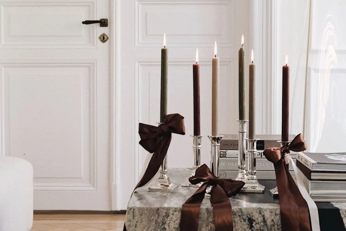 Tall candles in silver holders tied with brown satin bows, on a table beside a white panelled door