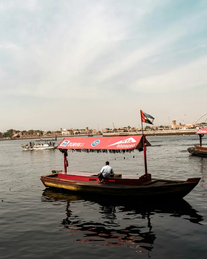 A wooden abra with a UAE flag crossing Dubai Creek, a man steering at the back