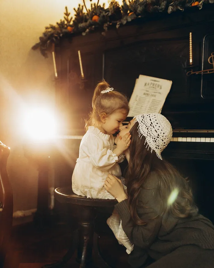 A small child holding a sheet of paper, kissing her mother on the cheek beside a piano
