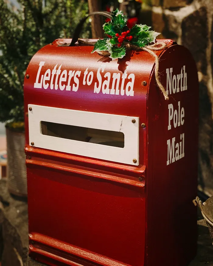 A red Letters to Santa postbox marked North Pole Mail, with holly on the lid