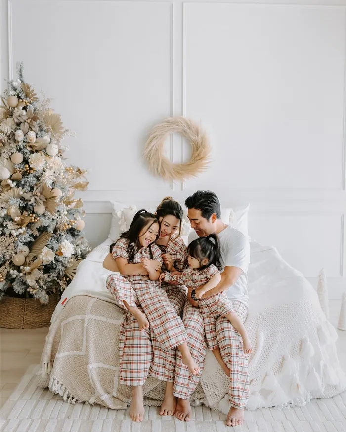 A family in matching checked pyjamas sitting close together on a white bed