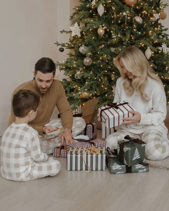 A family in matching pyjamas opening presents under a lit Christmas tree