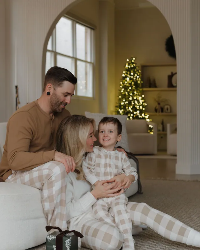 Parents and their small son in matching checked pyjamas sitting on the floor with a present
