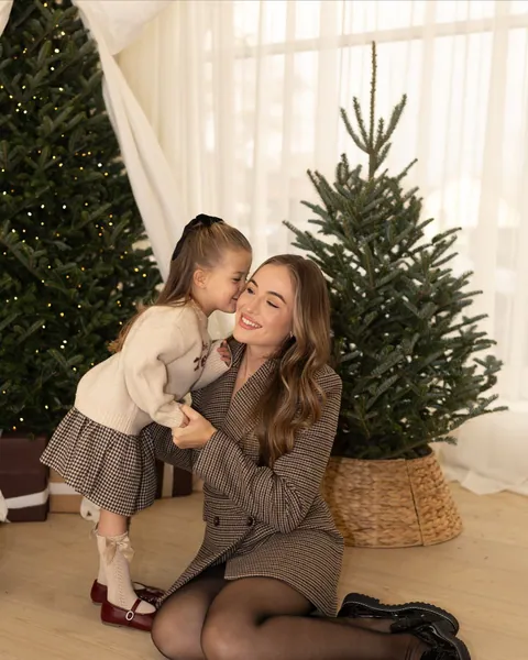 A small girl kissing her mother on the cheek as they sit on the floor beside a little Christmas tree