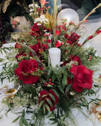 A low arrangement of red roses, berries and greenery around a white pillar candle