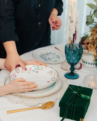 A floral plate on a pearl-edged charger beside a teal goblet, gold cutlery and a green velvet gift box