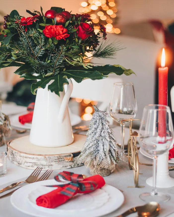 A white table laid for Christmas with red taper candles, tartan-tied red napkins and small frosted trees